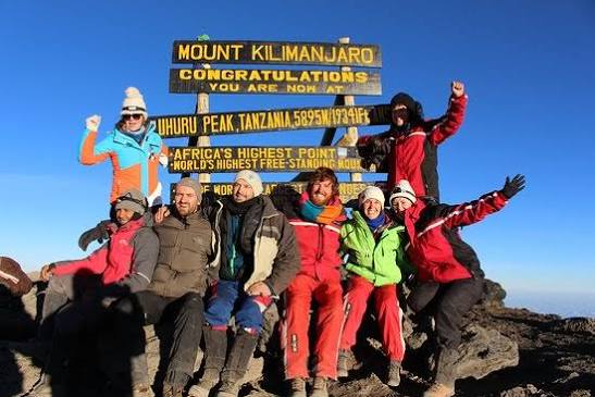 Proud trekkers celebrating on the roof of Africa at Uhuru Peak summit during a Mount Kilimanjaro climbing tour